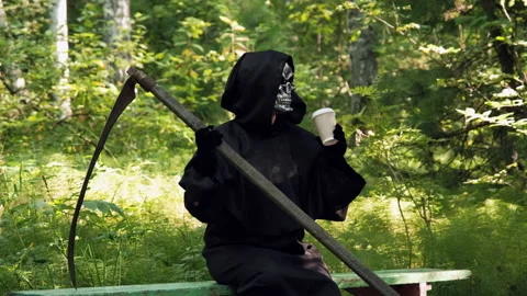 Grim Reaper with Scythe Drinking Coffee in a Park Stock Footage 136342735