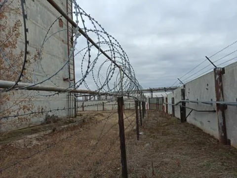Grim view of barbed wire and gray fence. Abandoned building. Ominous sky, clo Stock Photos