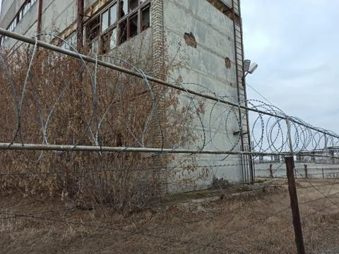 Grim view of barbed wire and gray fence. Abandoned building. Ominous sky, clo Stock Photos