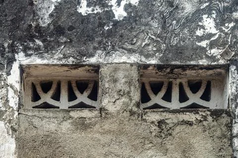 A grimy concrete wall features two weathered vents with an intricate, repea.. Stock Photos