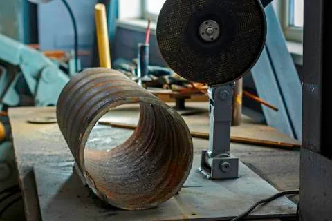A grinder with a disk on the workbench in the workshop and a large metal tube Stock Photos