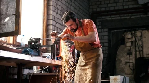 Grinding metal tools with sparkles - forge workshop Stock Footage 75647193