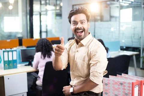 Grinning Employee Giving Thumbs Up While Standing In Office 스톡 사진