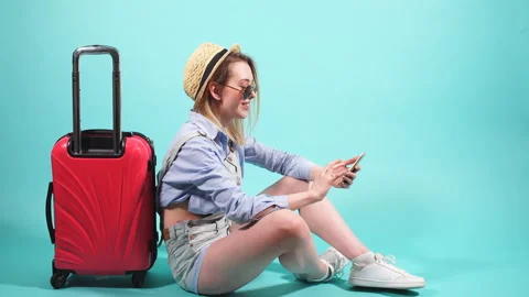 Grl with red suitcase on blue background using smartphone. Stock Footage 90387406