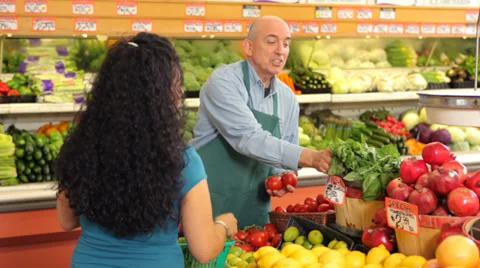 Grocery store worker helps woman shopping for produce Stock Footage