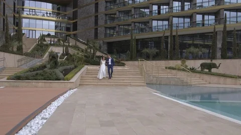 Groom and bride walking down the stairs on the luxury hotel territory near pool Stock Footage 94217671