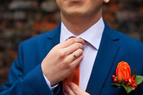 The groom in a blue suit adjusts his orange tie 库存照片