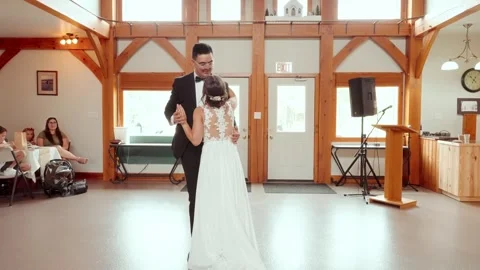Groom dips bride during first dance in rustic daytime venue as guests watch Stockbeeldmateriaal 320431918