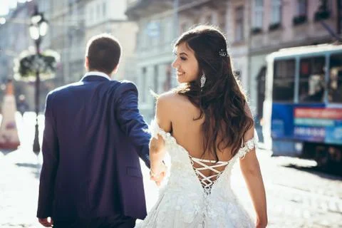 Groom is leading by the hand his adorable smiling brunette bride in the dress Stock Photos