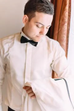 The groom is looking aside while standing near the window. Stock-Fotos