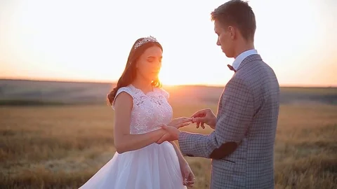 Groom putting a wedding ring on bride's finger. Wedding ceremony at sunset. Stock Footage 82844194