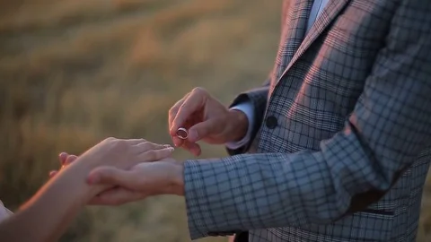 Groom putting a wedding ring on bride's finger. Wedding ceremony at sunset. Video stock 82844210