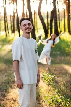 Groom smiling in forest with bride dancing in background on wedding day Stock Photos