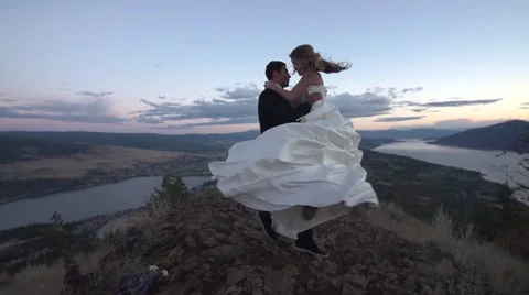 Groom Spins Bride in White Wedding Dress on a Mountain Top Stock Footage 67904649