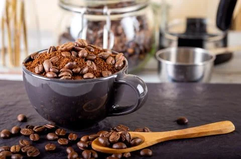 Ground black coffee in a black cup and several roasted coffee beans on top Stock Photos