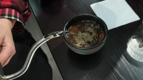 Ground coffee beans in cup receive boiling water poured from kettle Stock Footage 306600124