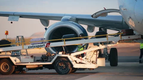 Ground crew loading luggage onto conveyor belt beside commercial jet engine. Stock Footage 337911289