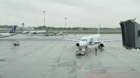 Ground crew pushing back airline plane with tug on wet airport tarmac Video stock 325031913
