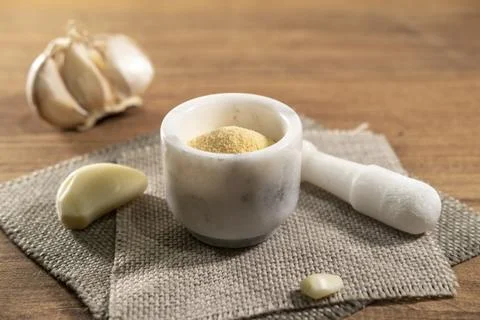 Ground dried garlic in small bowl and cloves on wooden background, spice garlic Stock Photos