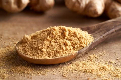 Ground ginger on a spoon with fresh ginger root in the background Stock Photos