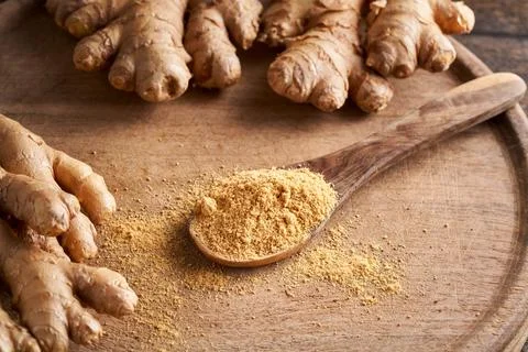 Ground ginger on a spoon with fresh ginger root in the background Stock Photos