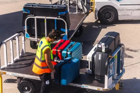 Ground Handler Loading Suitcases onto Airport Baggage Cart Stock Photos