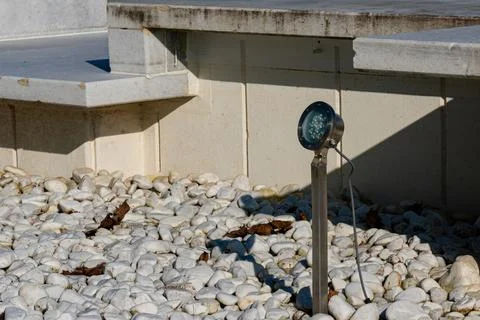 Ground-level garden light illuminates a pebble pathway in daylight Stock Photos