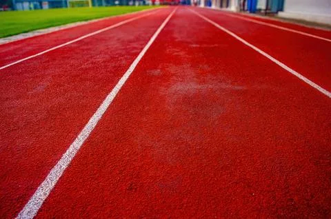Ground level view of red running track with white lane lines and grassy edg.. Stock Photos