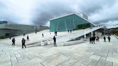 Ground level visitors sloping white marble roof oslo opera house angular glass Stock Footage 327635406