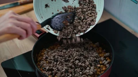 Ground meat is added to a pan containing chopped vegetables on a stove. Vidéo 337112897