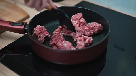 Ground meat is being cooked in a frying pan on a stovetop. Hands are stirring Видео 337112189