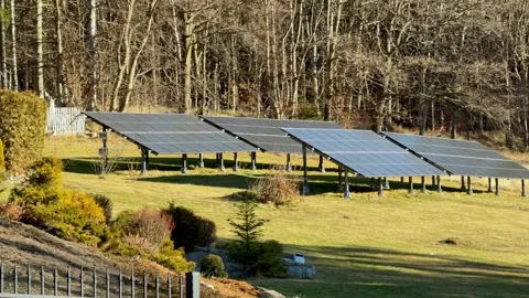 Ground-mounted solar panel array installed in a sunny backyard field near a Vídeo Stock 345822923