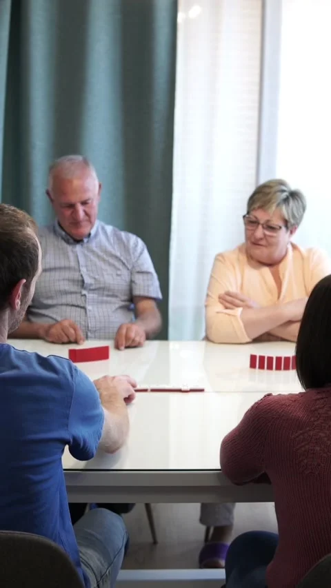 Group of 4 diverse people of all ages and genders play dominoes. Young man Stock Footage 220533730