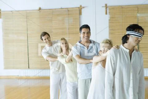 Group of adults standing single file holding onto each others' shoulders, leader Stock Photos