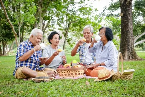 A group of Asian elders are sitting, relaxing and eating snacks in the garden. Photos