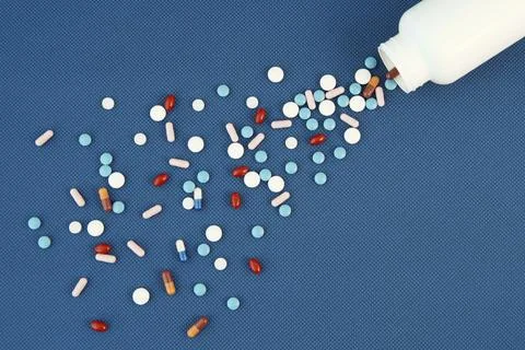 Group of assorted tablets and Capsules spilling out of white bottle. Blue Stock Photos