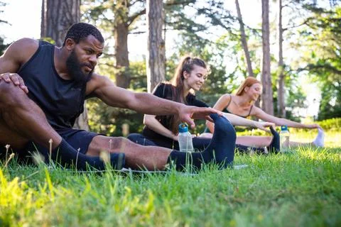 A group of athletes performs a stretching exercise sitting on a meadow Stock Photos