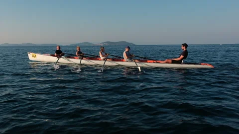 Group of athletes rowing together in a canoe on the sea with a city skyline in Stock Footage 345916984