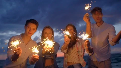Group of best friends having fun, standing on beach with sparklers light at Video stock 119161198