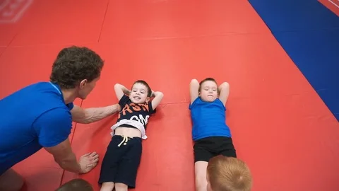 A group of boys performs an exercise for the abdominal muscles, the coach helps Video stock 102647216