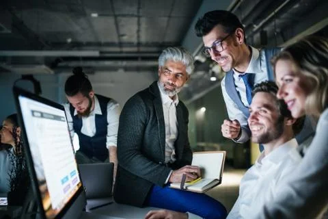 A group of business people in an office at night, using computer. Stock Photos