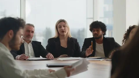 A group of businessmen sits at a large table in front of a window and Stock Footage 237760956