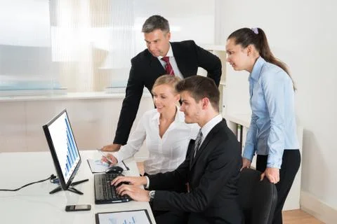 Group Of Businesspeople Looking At Graph On Computer In Office Stock Photos