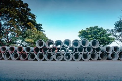 Group of cement tubes piled up on the side of a road by the tree Stock Photos