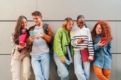 Group of cheerful teens using their smartphones while enjoying together, sharing Stock Photos