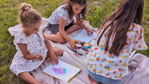 A group of children enjoy drawing on paper with crayons while sitting on a Stock Footage 341490839