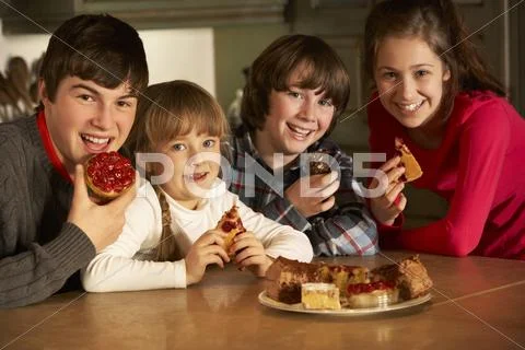 Group Of Children Enjoying Plate Of Cakes In Kitchen Stock Photos