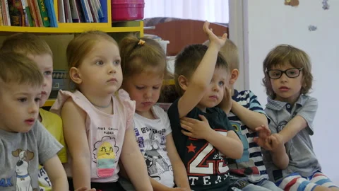 Group of children at kindergarten sitting on the bench and listening a teacher. Stock Footage 134016014