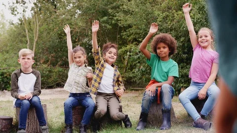 Group Of Children On Outdoor Activity Camping Trip Sitting Around Camp Fire With Stock Footage 124570142