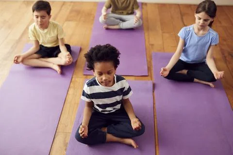 Group Of Children Sitting On Exercise Mats And Meditating In Yoga Studio Stock Photos